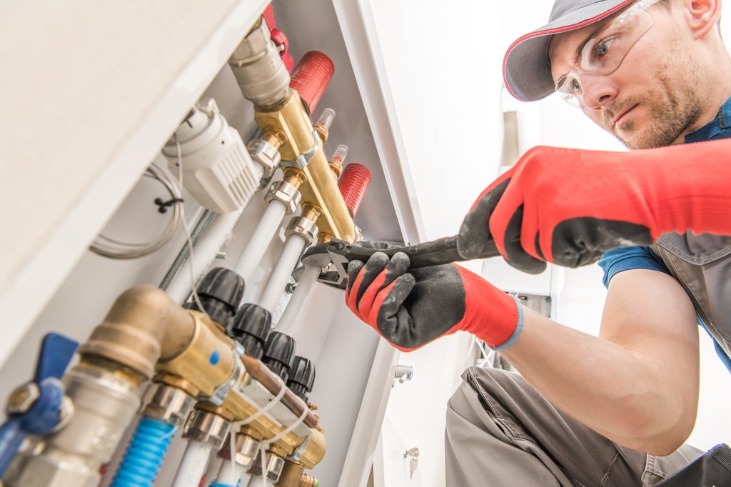A licensed plumber replacing a heavily corroded cast iron vertical soil stack with modern white PVC piping inside an exposed wall cavity in a Philadelphia rowhome.